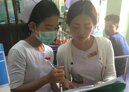Two health professionals, one in face mask, review notes in a busy hospital setting