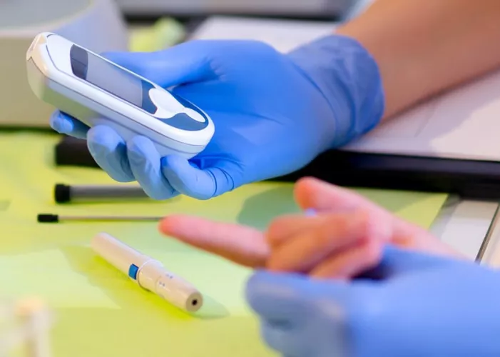 Close up of gloved hands taking blook prick sample of someone else's hands
